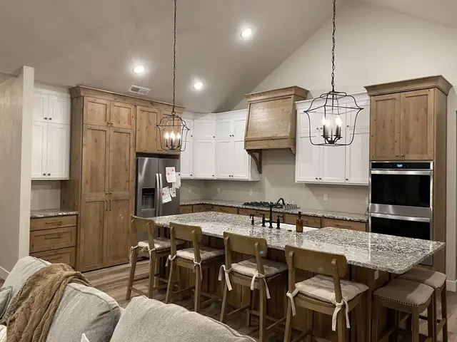 Long granite-topped island with bar stools in an open kitchen with wood and white cabinets