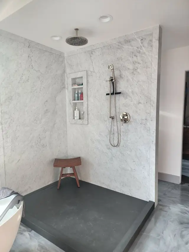 Walk-in shower lined with large white veined stone slabs, a built-in niche and a handheld shower