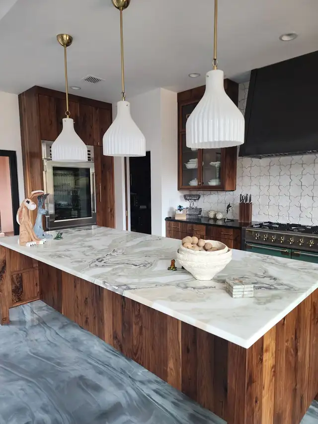 Long walnut island with white and green veined natural stone top under white ribbed pendant lights