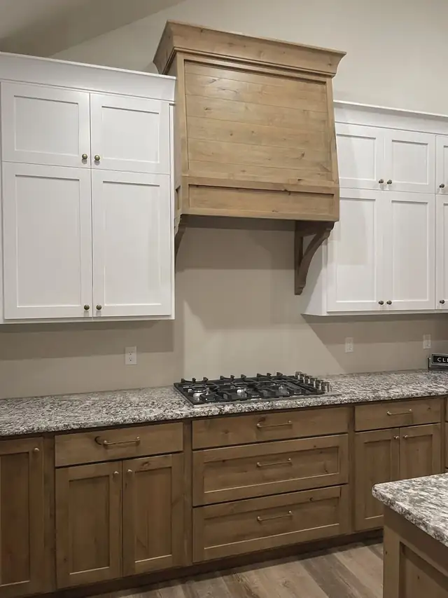 Speckled granite countertop under white cabinets with a gas cooktop and wood range hood