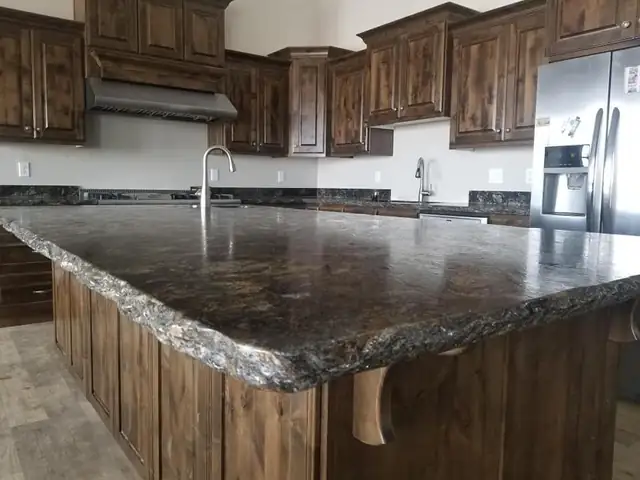 Large island with dark brown and gold granite top and chiseled edge, set on knotty alder cabinets