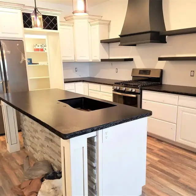 Black countertop on a white island with undermount sink, white cabinets and a wine fridge